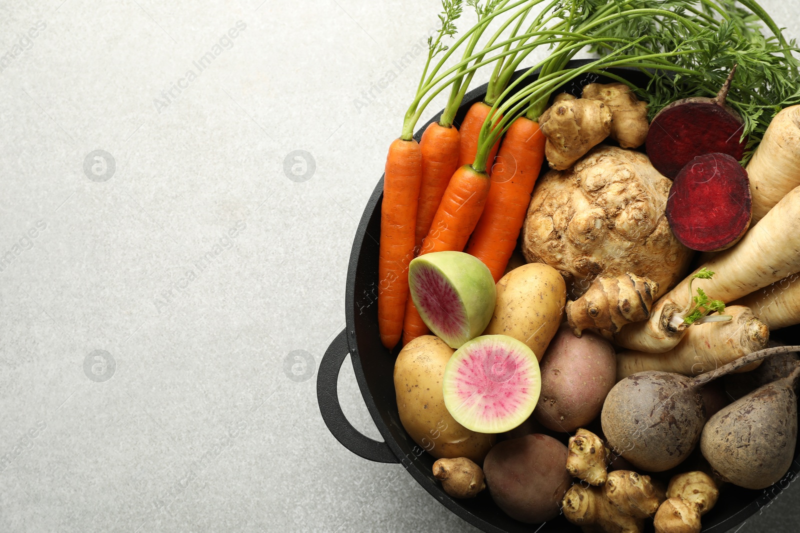 Photo of Different root vegetables in pot on light grey table, top view. Space for text