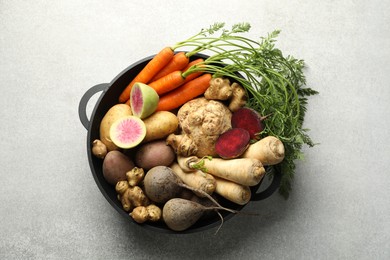 Photo of Different root vegetables in pot on light grey table, top view