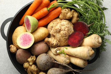 Photo of Different root vegetables in pot on light grey table, top view