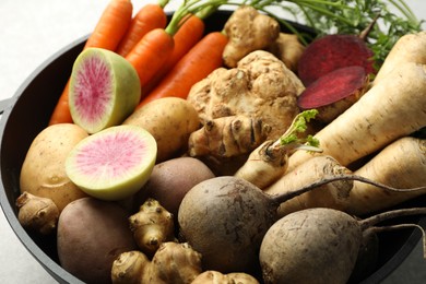 Photo of Different root vegetables in pot on light grey table, closeup