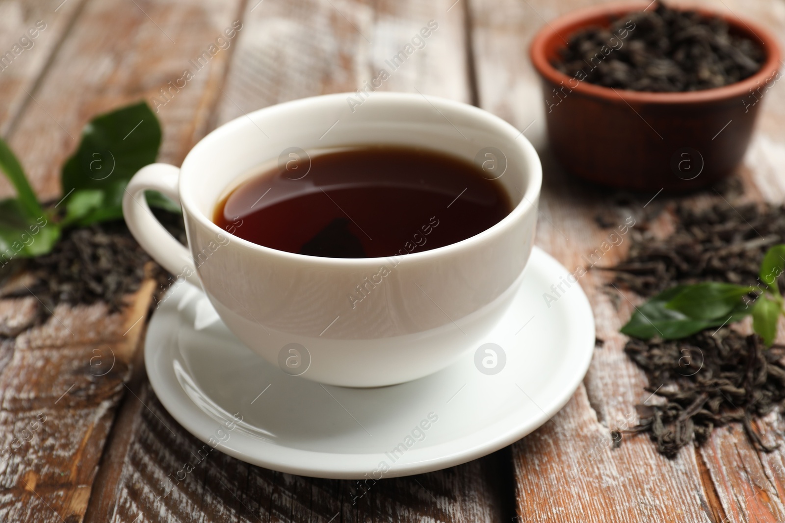 Photo of Aromatic tea, brew and fresh leaves on wooden table, closeup