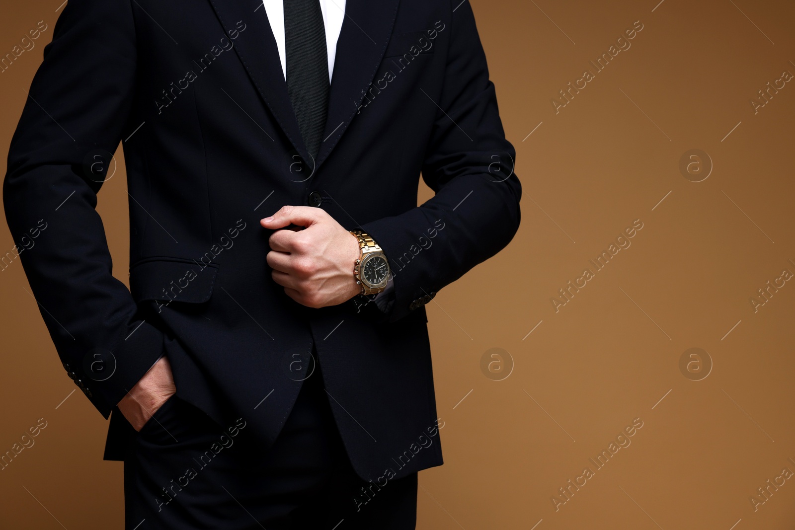 Photo of Man in classic suit with stylish watch on brown background, closeup. Space for text