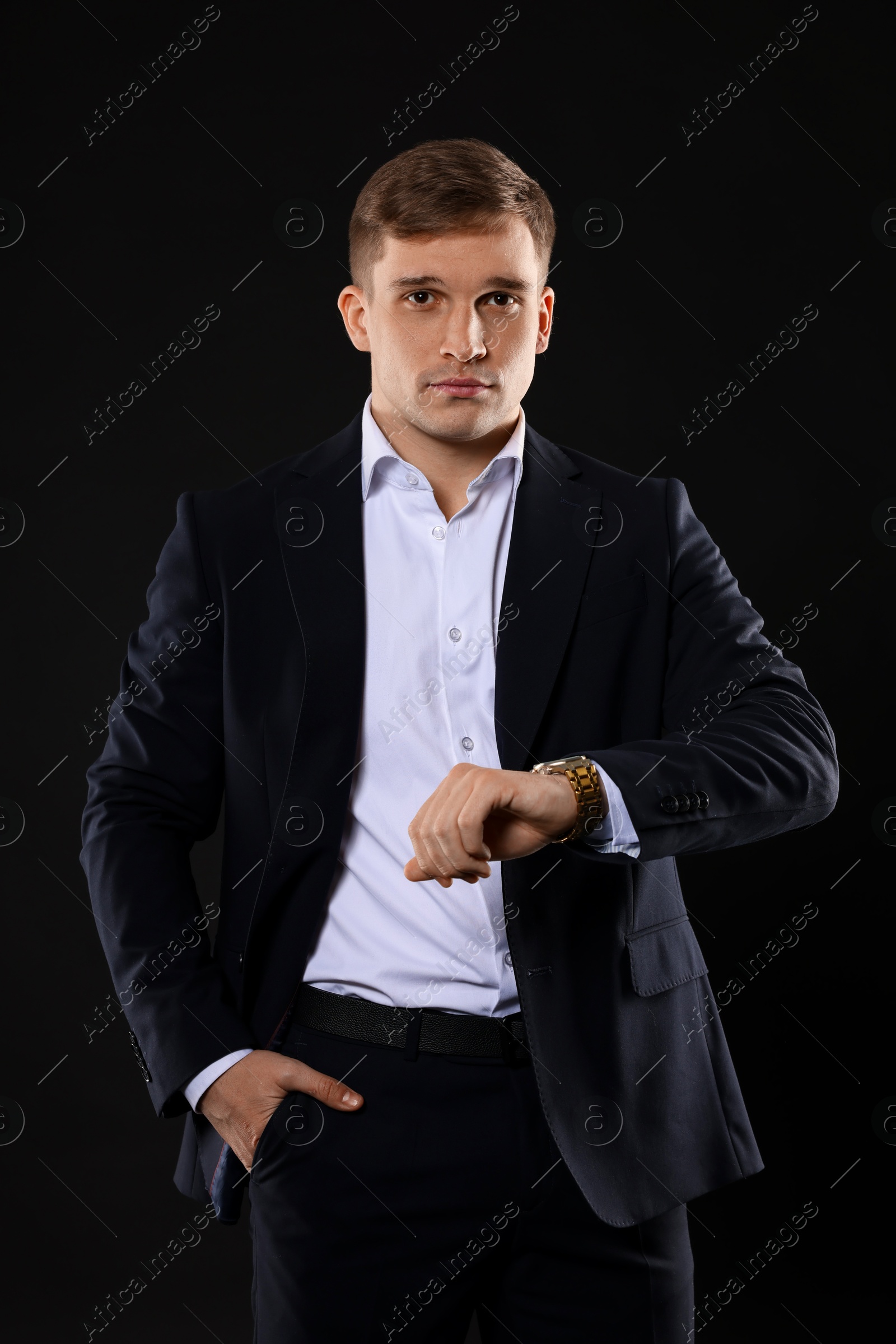 Photo of Man in classic suit checking time on black background