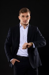 Photo of Man in classic suit checking time on black background