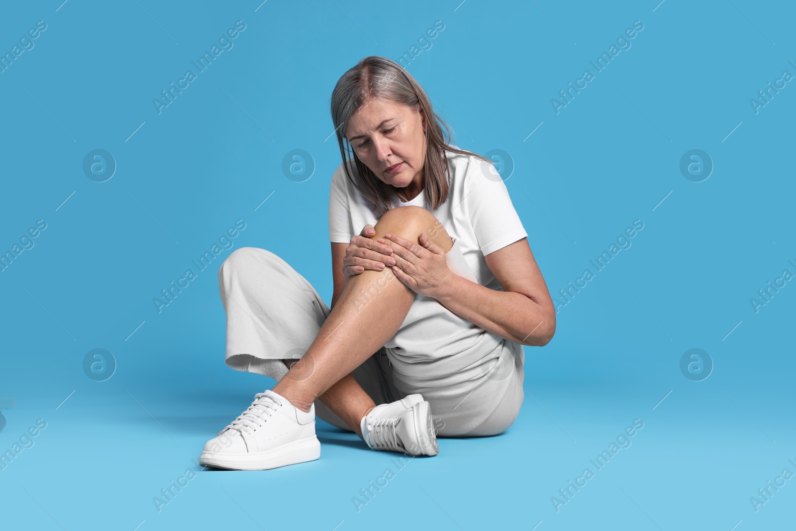 Photo of Senior woman suffering from knee pain on light blue background