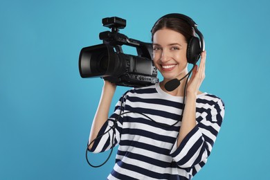 Happy woman with professional video camera and headset on light blue background