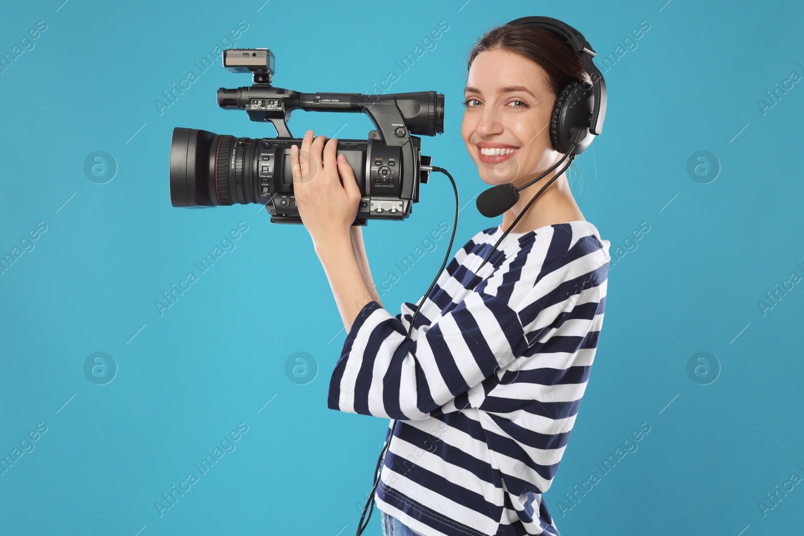 Photo of Happy woman with professional video camera and headset on light blue background