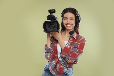 Photo of Happy woman with professional video camera and headset on pale olive background