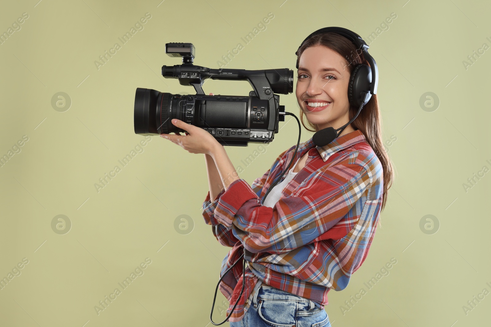 Photo of Happy woman with professional video camera and headset on pale olive background