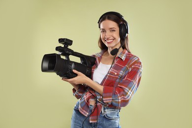 Photo of Happy woman with professional video camera and headset on pale olive background