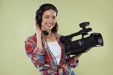 Photo of Happy woman with professional video camera and headset on pale olive background