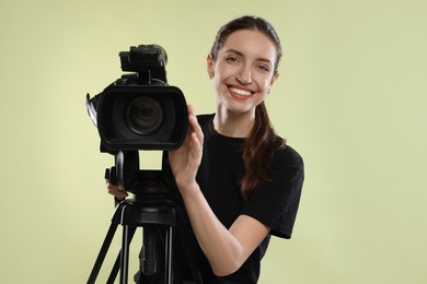 Photo of Happy woman with professional video camera on pale olive background