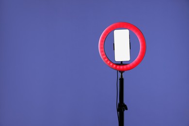 Photo of Ring lamp with smartphone on purple background, space for text