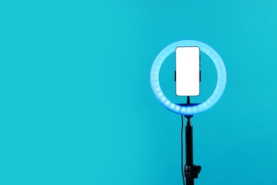 Photo of Ring lamp with smartphone on light blue background, space for text