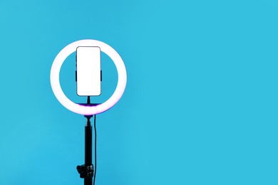 Photo of Ring lamp with smartphone on light blue background, space for text