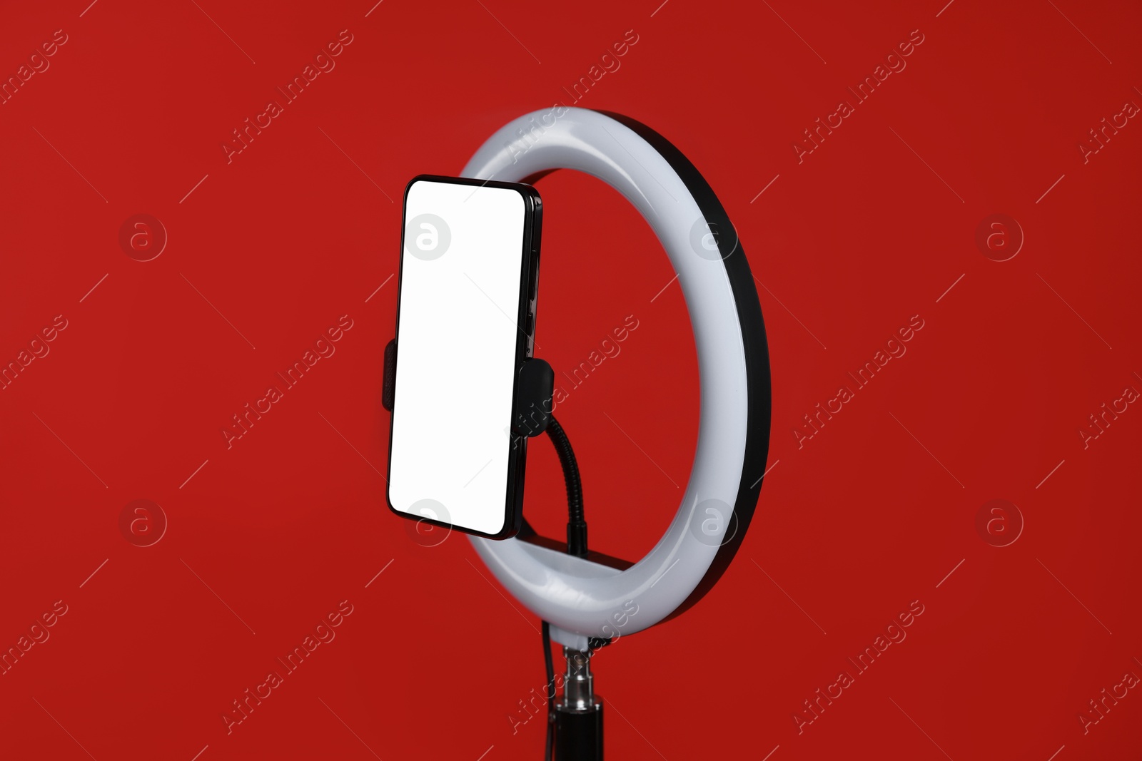 Photo of Ring lamp with smartphone on red background, closeup