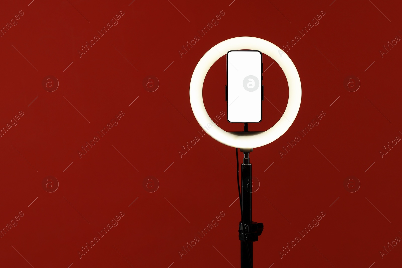 Photo of Ring lamp with smartphone on red background, space for text