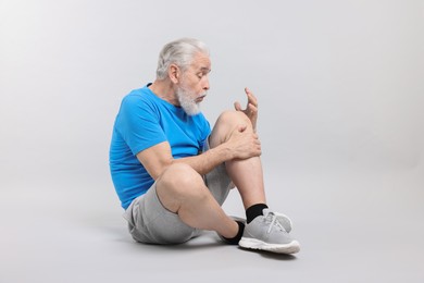 Photo of Senior man suffering from knee pain on light grey background