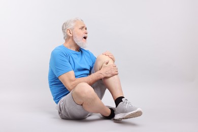 Photo of Senior man suffering from knee pain on light grey background. Space for text