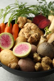 Photo of Different root vegetables in pot on light grey table, closeup