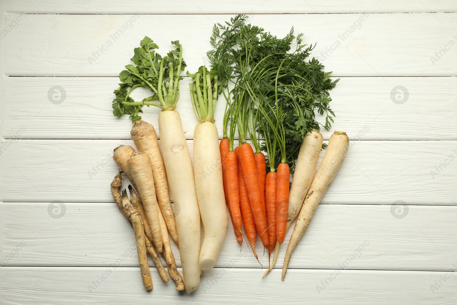 Photo of Different root vegetables on white wooden table, flat lay