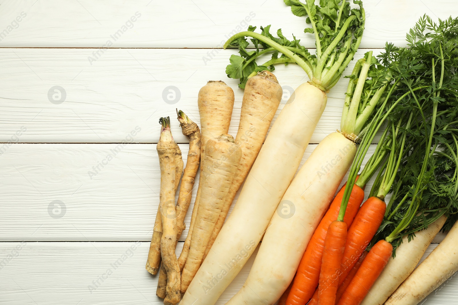 Photo of Different root vegetables on white wooden table, flat lay. Space for text