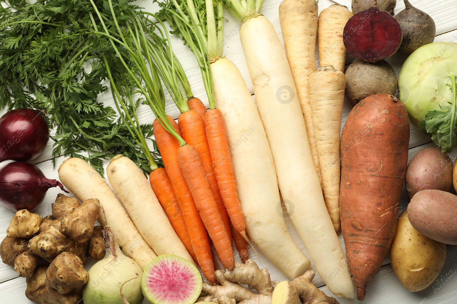 Photo of Different root vegetables on white wooden table, flat lay