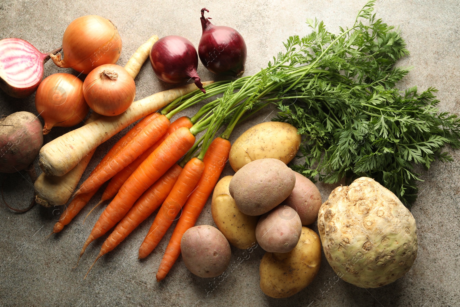 Photo of Different root vegetables on grey table, flat lay