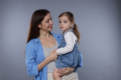 Happy mother with her cute little daughter on grey background