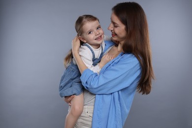 Happy mother with her cute little daughter on grey background