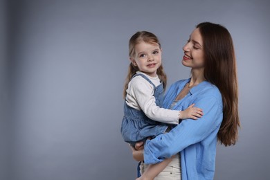 Happy mother with her cute little daughter on grey background, space for text