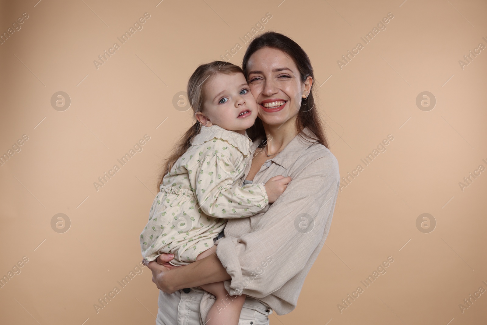 Photo of Portrait of happy mother with her cute little daughter on beige background