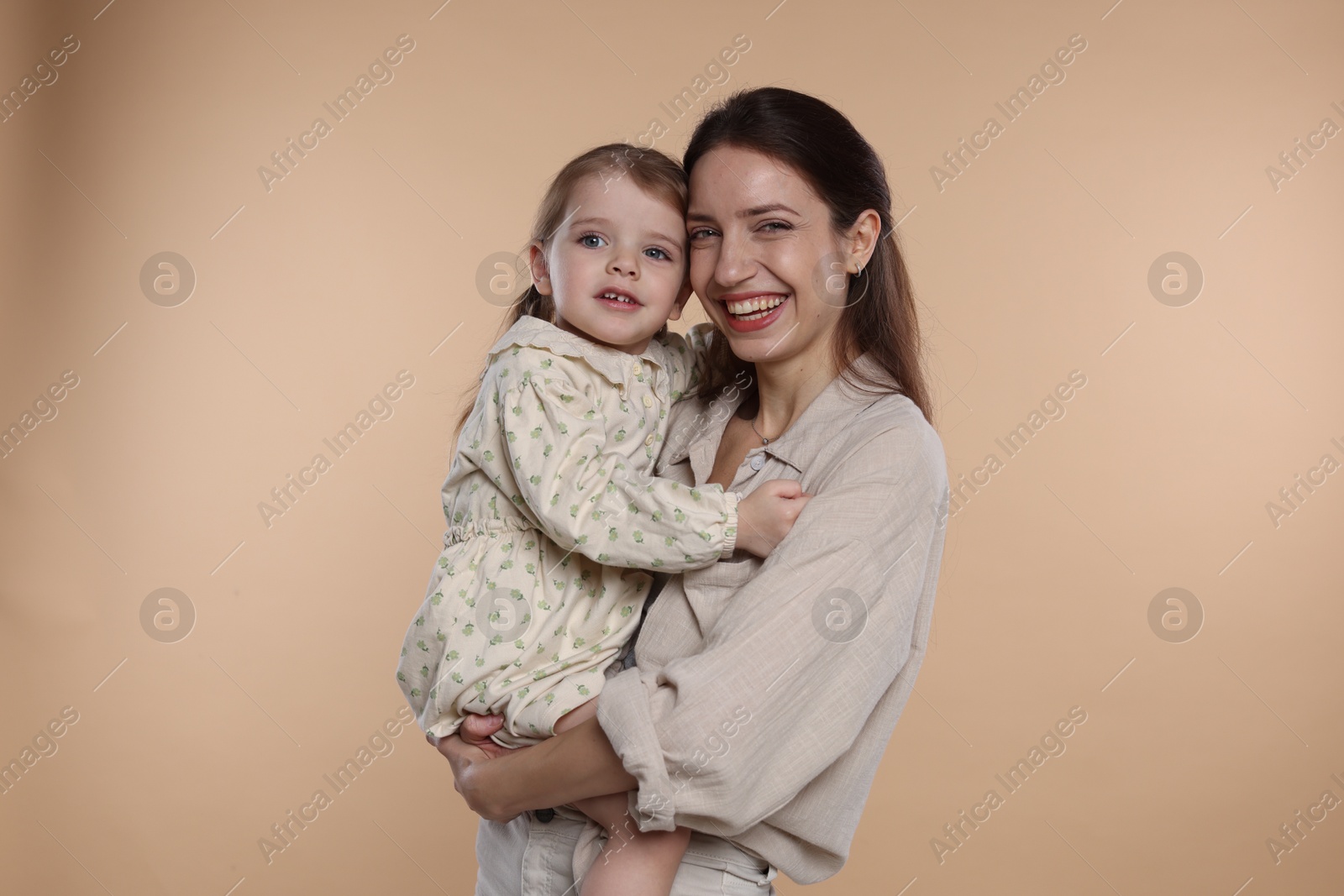 Photo of Portrait of happy mother with her cute little daughter on beige background