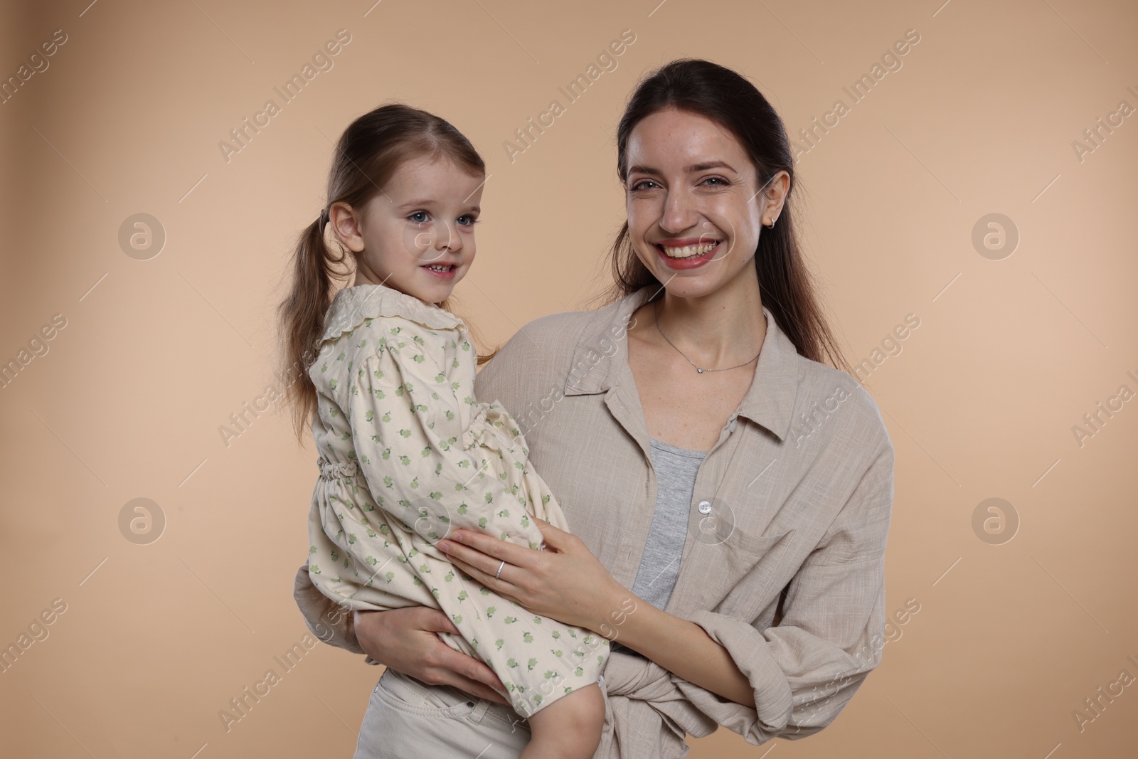 Photo of Portrait of happy mother with her cute little daughter on beige background