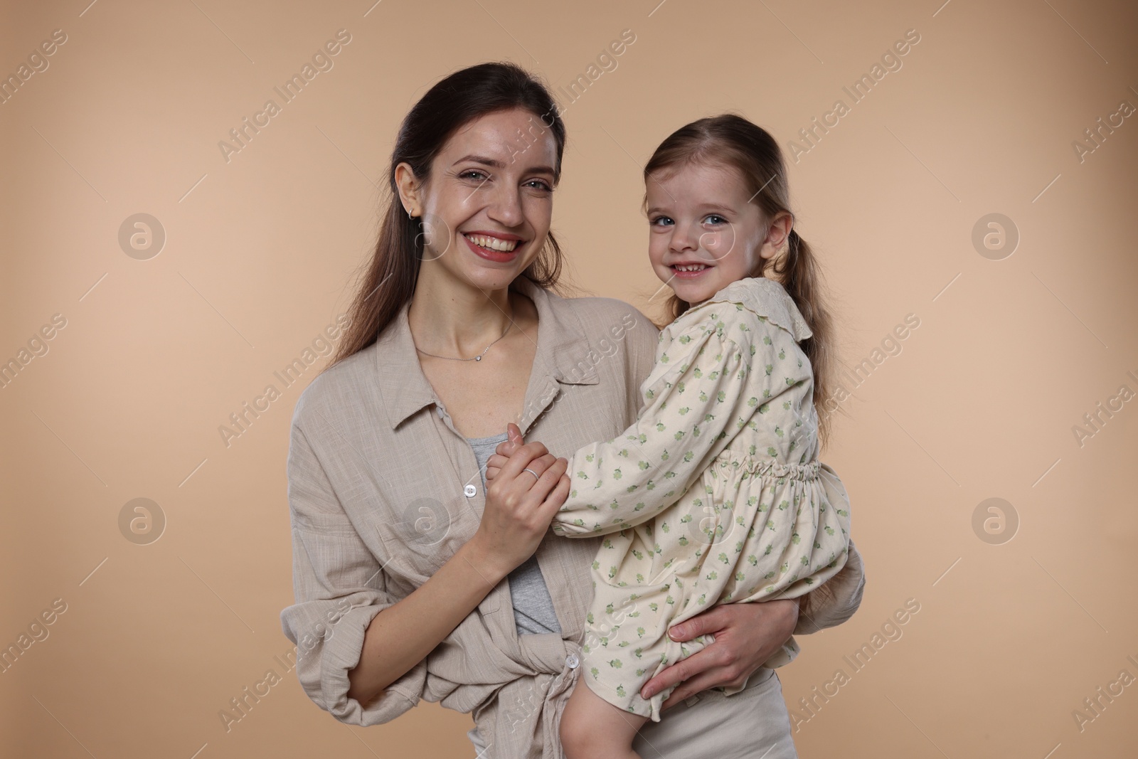 Photo of Portrait of happy mother with her cute little daughter on beige background