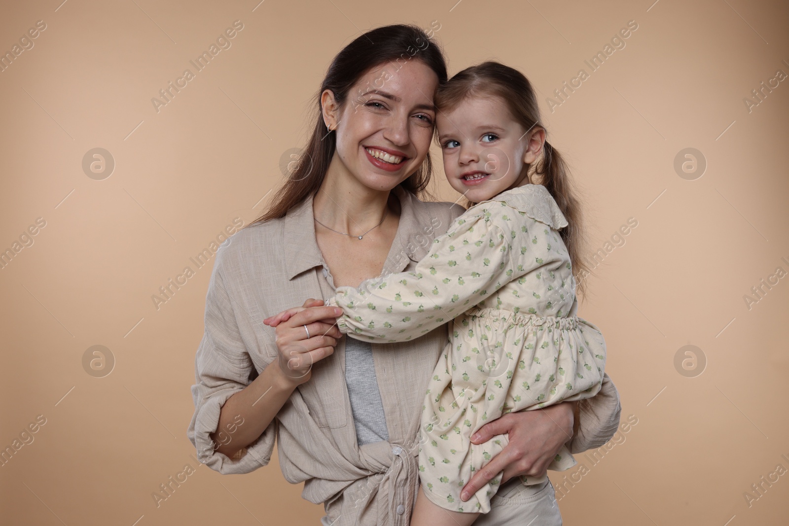 Photo of Portrait of happy mother with her cute little daughter on beige background