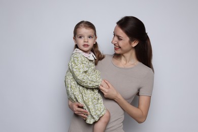 Happy mother with her cute little daughter on grey background