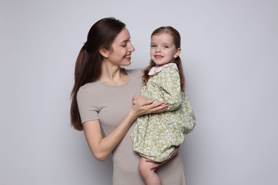 Happy mother with her cute little daughter on grey background