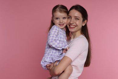 Portrait of happy mother with her cute little daughter on pink background