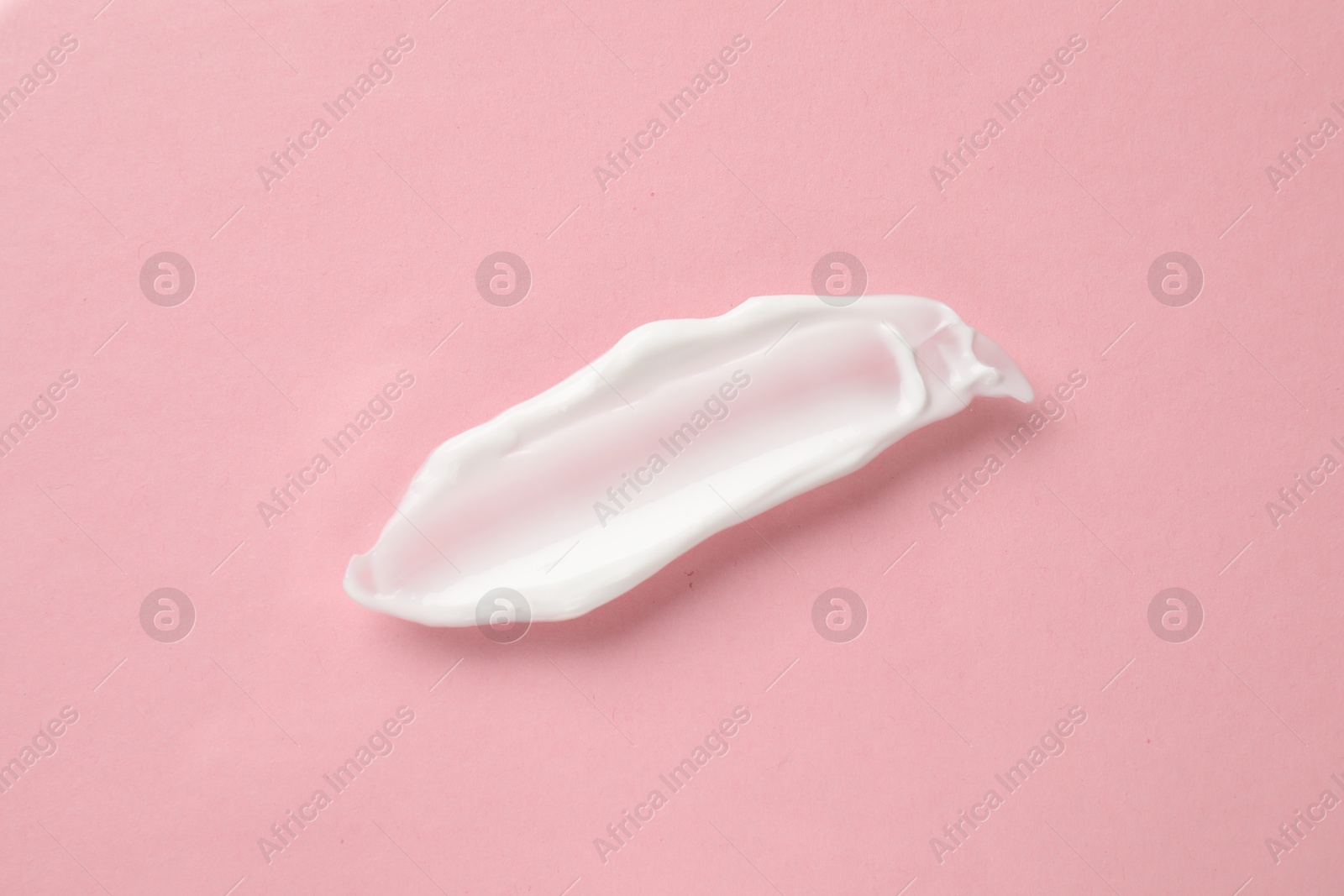 Photo of Smear of body cream on light pink background, top view