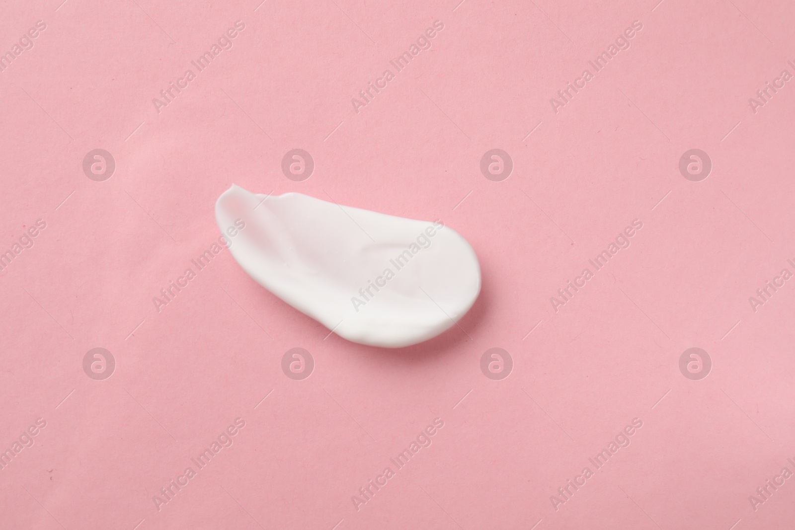 Photo of Smear of body cream on light pink background, top view