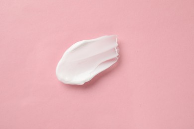 Photo of Smear of body cream on light pink background, top view