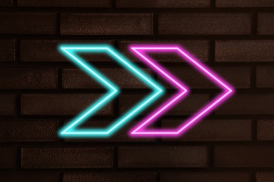 Image of Bright neon arrow-shaped pointer on brick wall