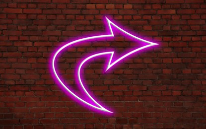 Image of Pink neon arrow-shaped pointer on brick wall