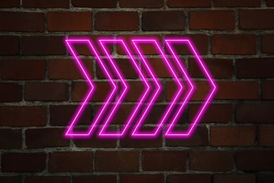 Image of Pink neon arrow-shaped pointer on brick wall