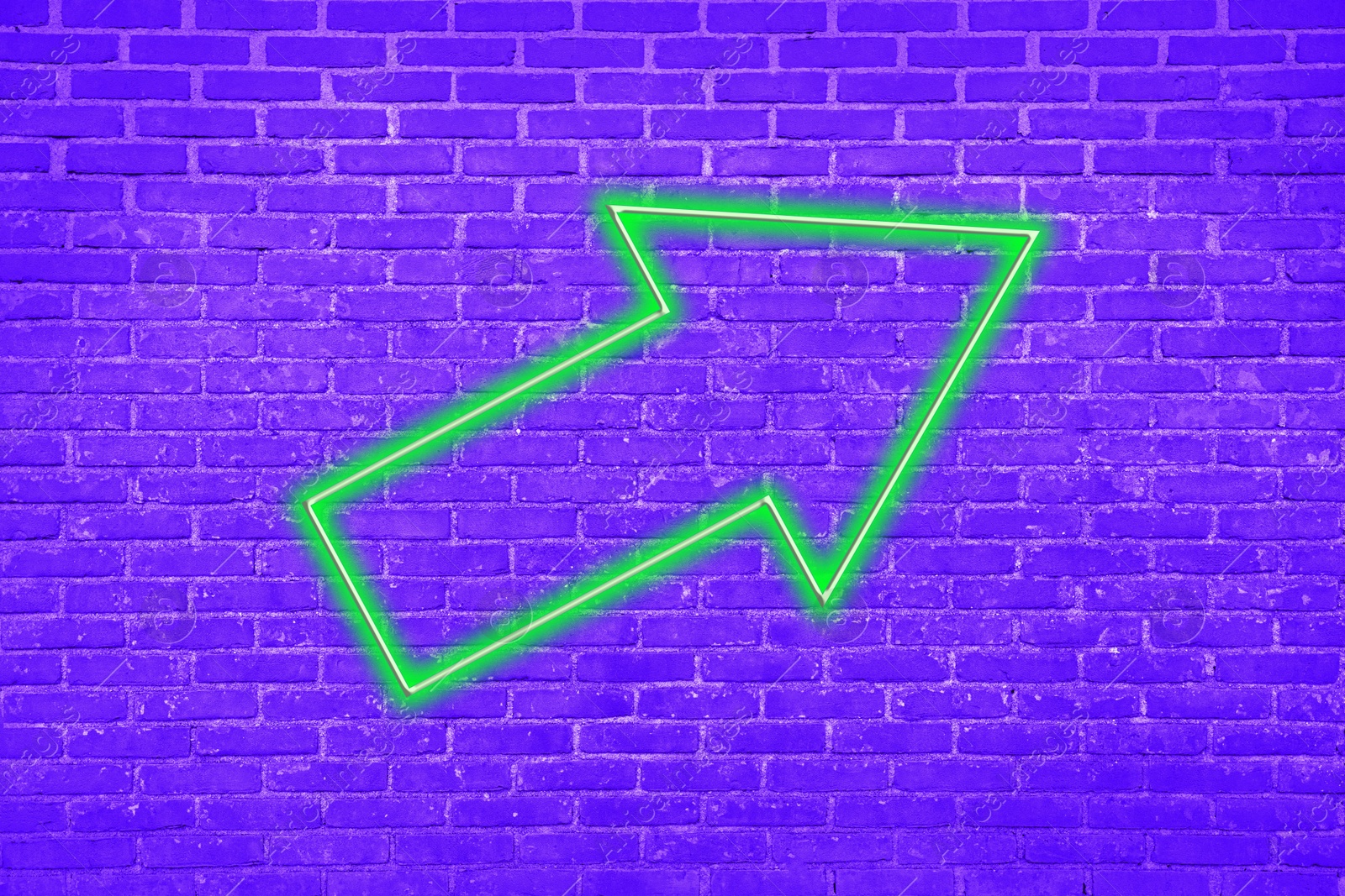 Image of Green neon arrow-shaped pointer on brick wall