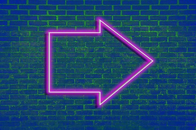 Image of Pink neon arrow-shaped pointer on blue brick wall