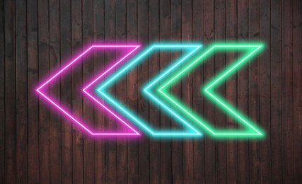 Image of Bright neon arrow-shaped pointer on wooden wall