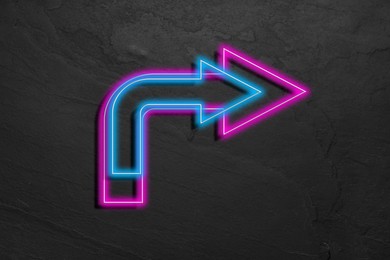 Image of Bright neon arrow-shaped pointer on grey textured wall