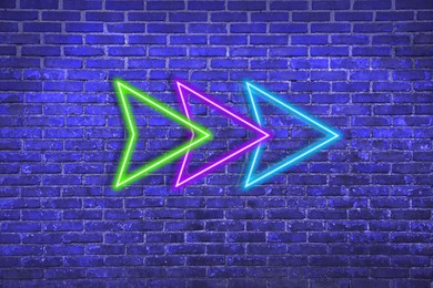 Image of Bright neon arrow-shaped pointer on blue brick wall